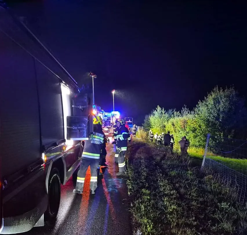 Feuerwehrleute in Schutzkleidung stehen um einen Feuerwehrwagen auf einer dunklen Straße in der Nacht.