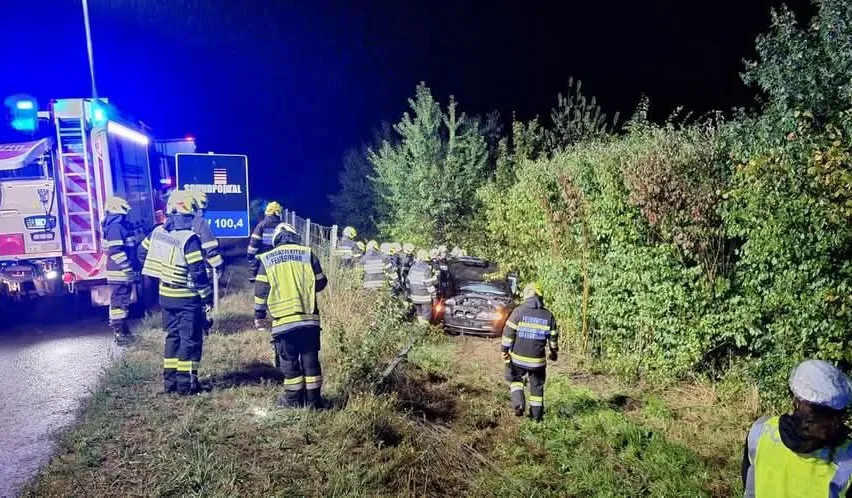 Rettungskräfte kümmern sich um einen Autounfall bei Nacht. Das Auto ist von der Straße abgekommen und Feuerwehrleute untersuchen das Fahrzeug.