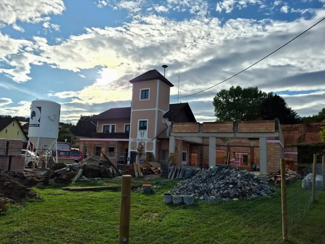 Eine Baustelle mit einem im Bau befindlichen Gebäude, das einen Turm und einen Schutthaufen aufweist. Der Himmel ist blau mit Wolken.