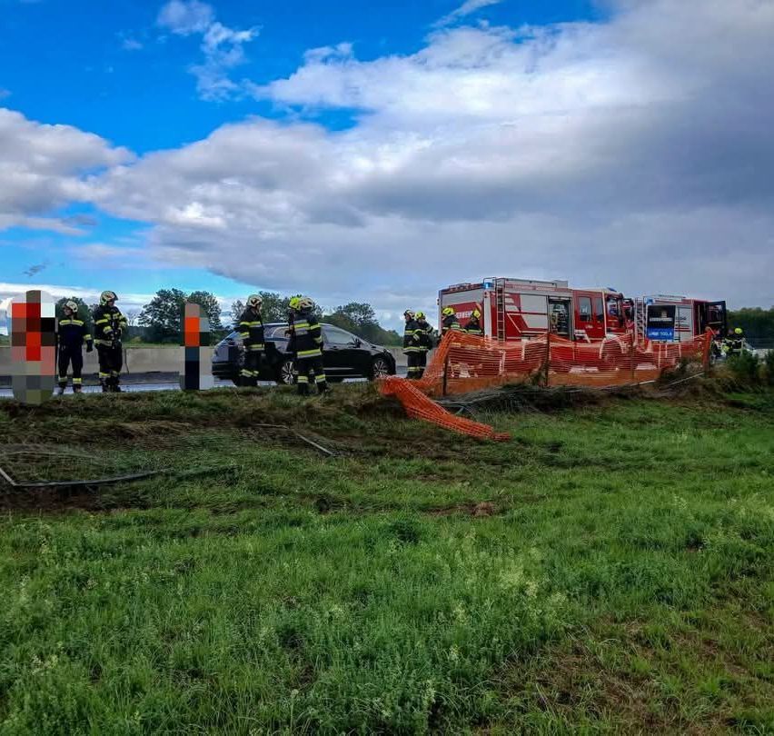 Feuerwehrleute stehen neben einem demolierten Auto auf einem Grasfeld unter einem bewölkten Himmel.