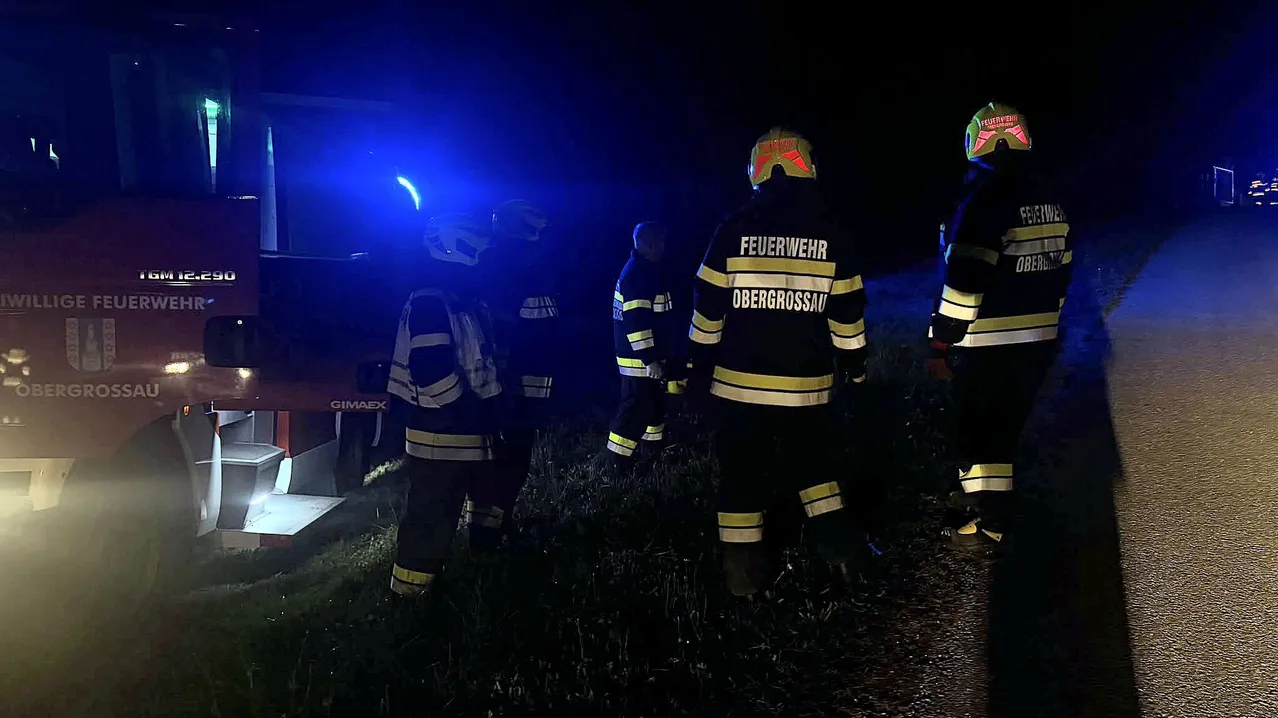 Eine Gruppe von Feuerwehrleuten in voller Ausrüstung geht bei Nacht auf einer Straße, mit einem geparkten Feuerwehrwagen an der Seite.