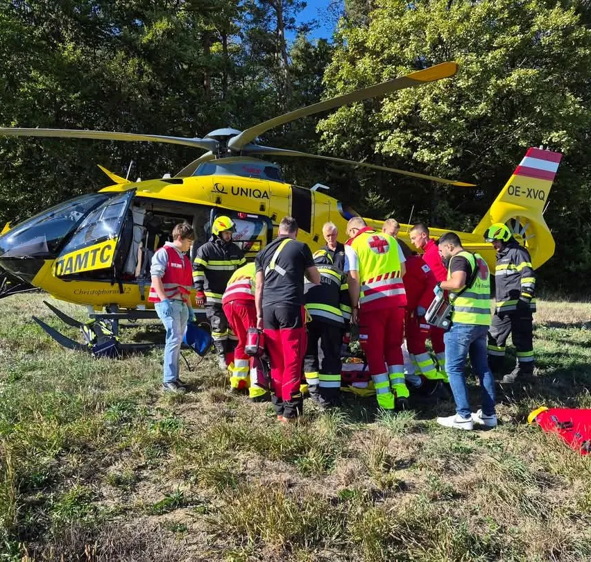Eine Gruppe von Rettungskräften kümmert sich um einen Patienten am Boden in der Nähe eines gelben Hubschraubers.