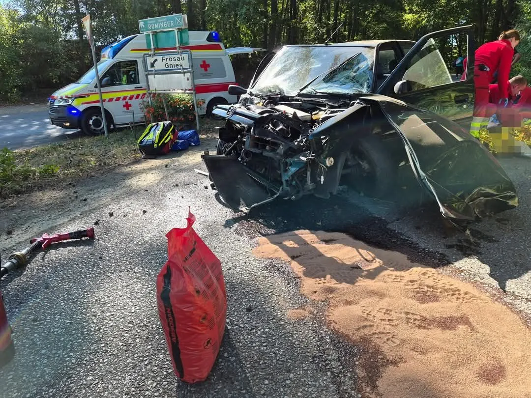 Ein Unfallort mit einem beschädigten Auto, einem Krankenwagen und Rettungspersonal.