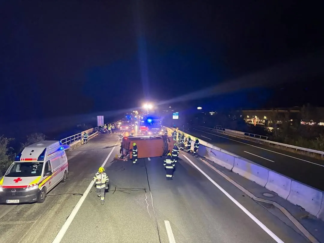 Eine nächtliche Szene einer umgestürzten LKW auf einer Autobahn, wobei Rettungskräfte die Situation behandeln.