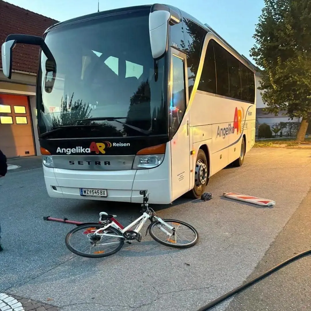 Ein weißer Bus mit dem Namen Angelika Reisen ist am Straßenrand geparkt. Ein Fahrrad liegt vor dem Bus auf dem Boden.