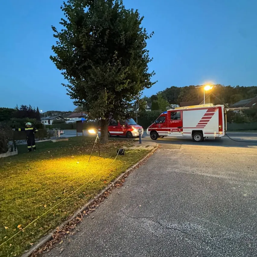 Ein Feuerwehrauto ist nachts am Straßenrand geparkt. Ein Mann in einer Feuerwehruniform steht neben einem Baum.