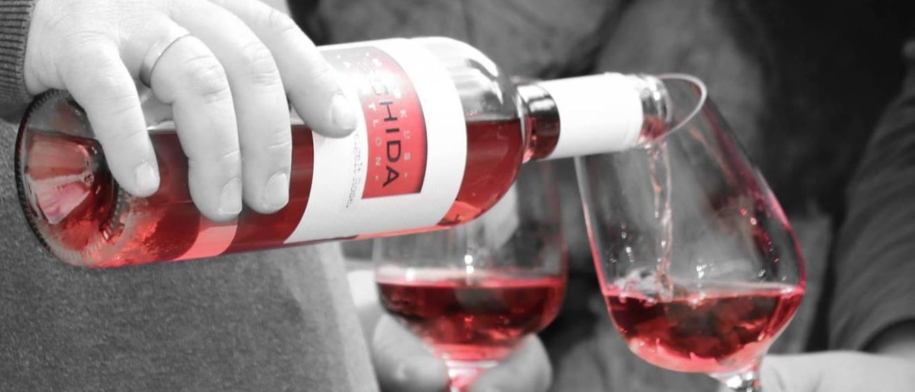 Eine Person gießt roten Wein aus einer Flasche in zwei Weingläser, die von zwei anderen Personen gehalten werden.