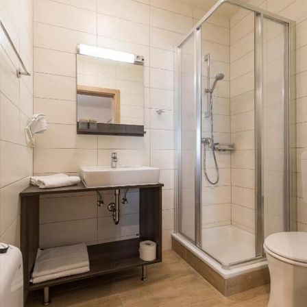 Ein Badezimmer mit Dusche, Waschbecken und Toilette. Die Wände und der Boden sind gefliest. Handtücher liegen auf der Theke.