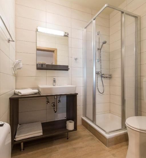 Ein Badezimmer mit Dusche, Waschbecken und Toilette. Die Wände und der Boden sind gefliest. Handtücher liegen auf der Theke.