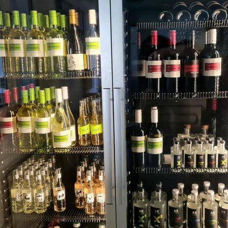 Zwei Kühlschränke mit Glastüren, die verschiedene Weinflaschen zeigen, einschließlich Rot-, Weiß- und Sektweinen, sowie einige Spirituosenflaschen. Die Kühlschränke haben Regale aus Edelstahl und einen schwarzen Hintergrund.