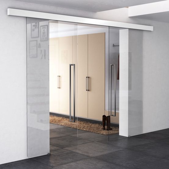 Ein modernes Zimmer mit einer Glasschiebetür und zwei Schränken mit Metallgriffen. Ein Teppich liegt auf dem Boden mit Stiefeln.