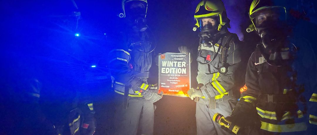 Drei Feuerwehrleute tragen Helme und halten ein Schild für die Winter-Edition-Veranstaltung hoch, wobei blaue Lichter die Szene beleuchten.