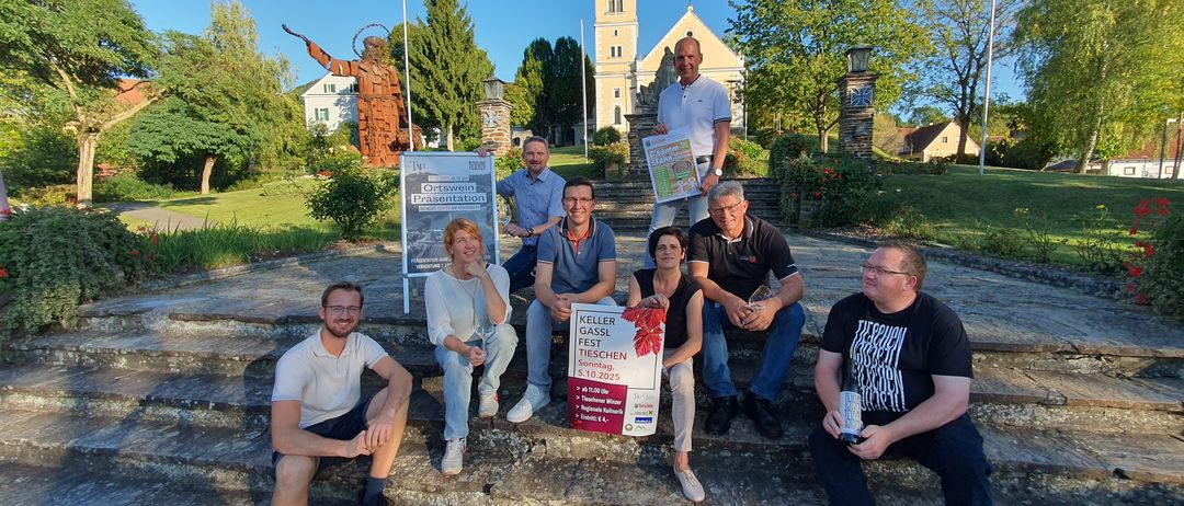 Eine Gruppe von Menschen posiert für ein Foto auf Steinstufen vor einer Kirche, hält ein Plakat und eine Karte.