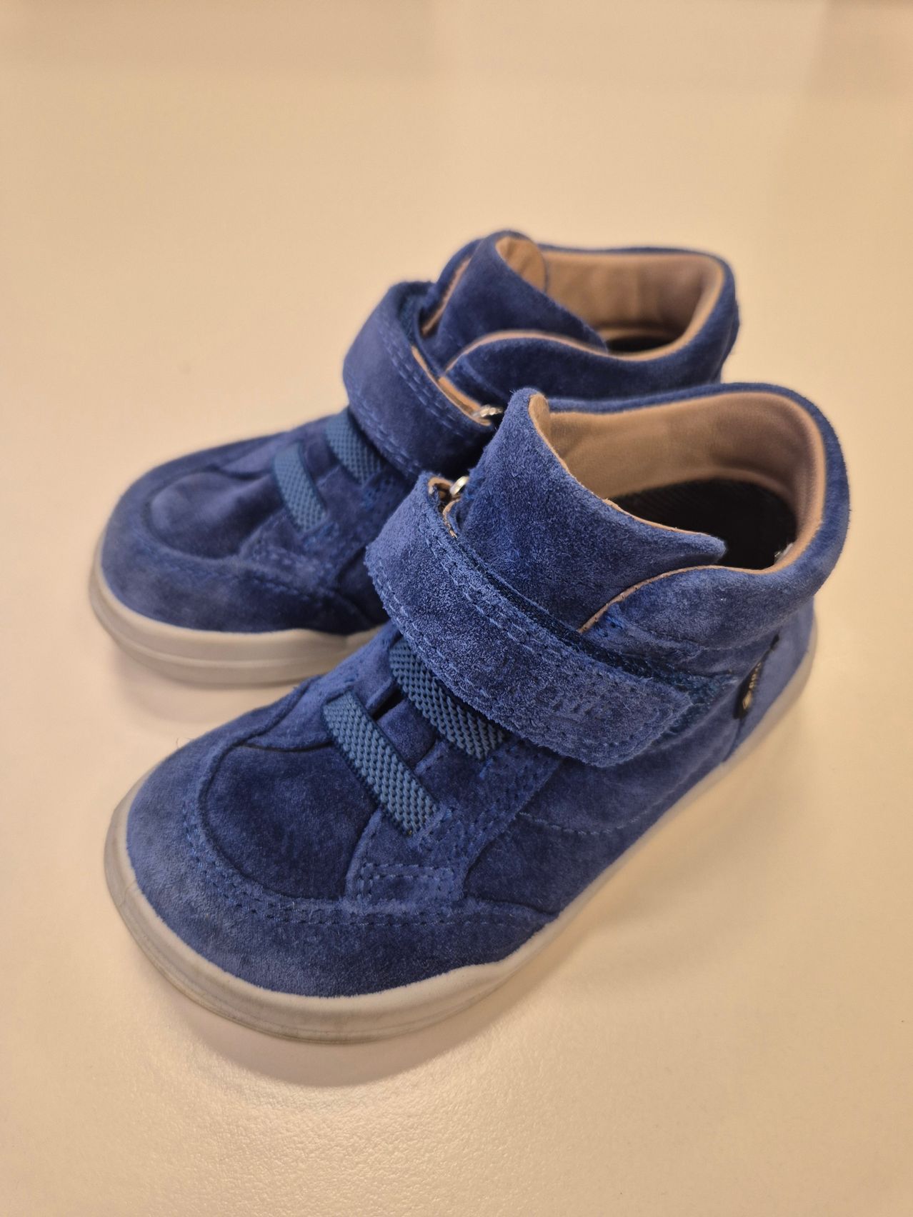 Ein Paar blaue Wildlederstiefel mit Reißverschlüssen und weißen Sohlen wird auf einem hellen Hintergrund gezeigt.
