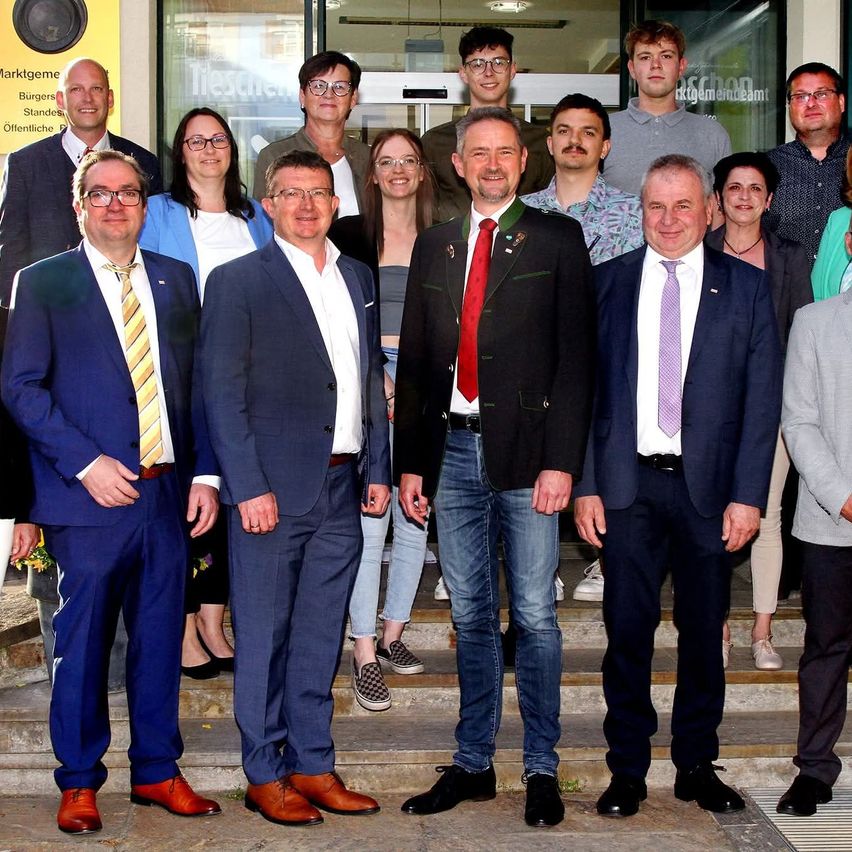 Eine Gruppe formell gekleideter Personen, darunter Männer und Frauen, steht auf Stufen vor einem Gebäude und lächelt für ein Foto.