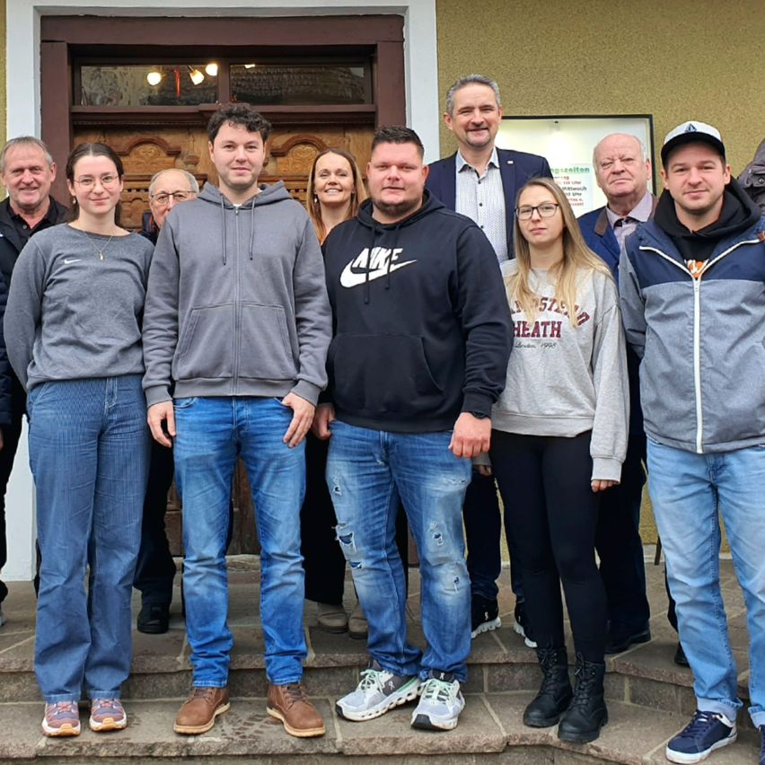 Eine Gruppe von Personen steht auf Stufen vor einem Gebäude. Sie lächeln und posieren für ein Foto. Die Personen tragen Freizeitkleidung.