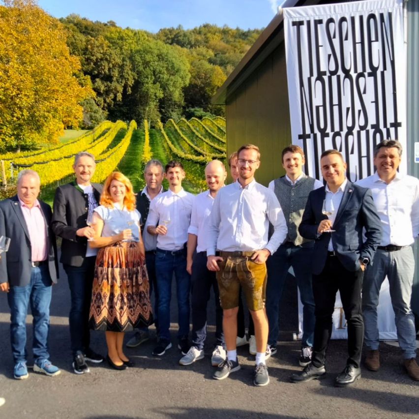 Gruppe von Menschen in formeller Kleidung, die vor einem Weinberg für ein Foto posieren.