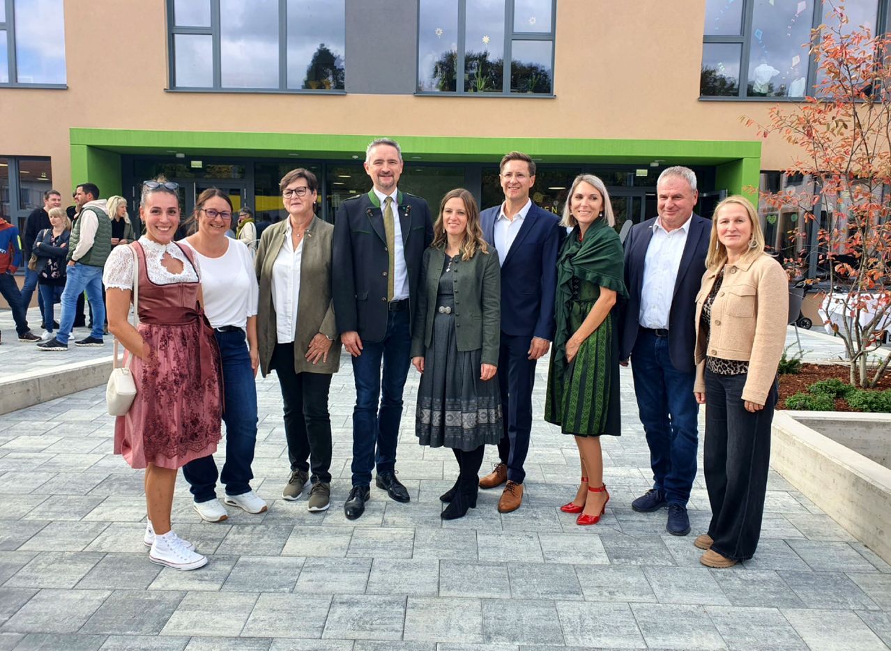 Eine Gruppe von Erwachsenen in formeller Kleidung steht vor einem Gebäude mit Glasfenstern.