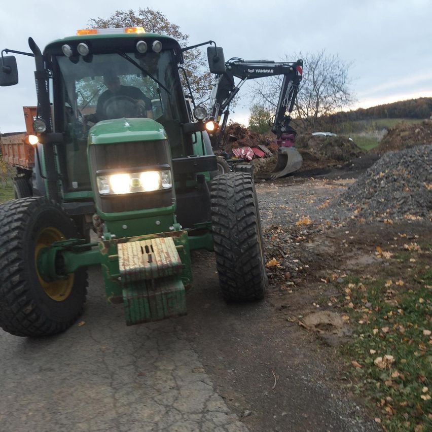 Ein grüner Traktor ist auf einer Kiesstraße geparkt, mit einer gelben Lampe und einer Person auf dem Fahrersitz.