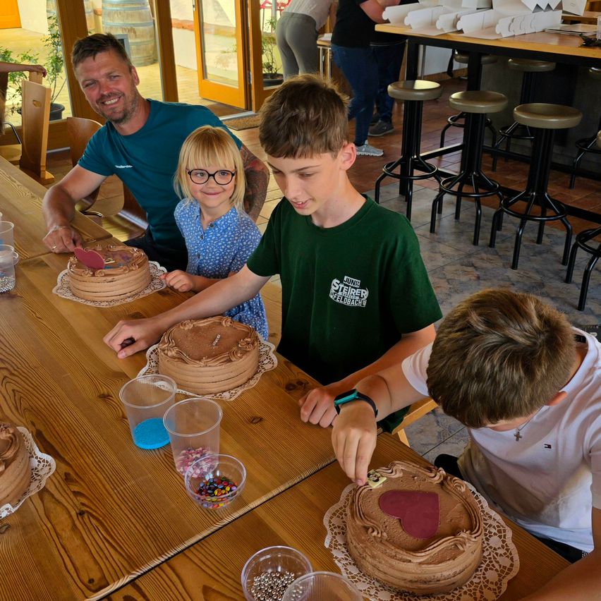 Eine vierköpfige Familie verziert Schokoladenkuchen an einem Tisch. Ein Junge legt Streusel und Süßigkeiten auf einen Kuchen.