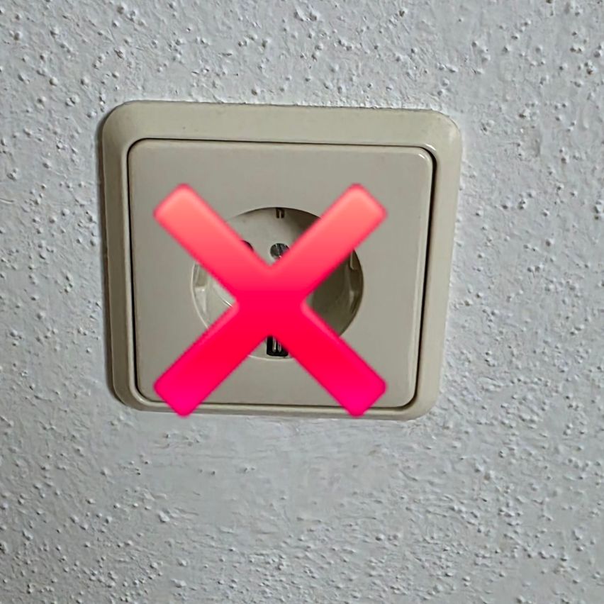 A white electrical socket is mounted on a wall with a red 'X' mark indicating it is not in use.
