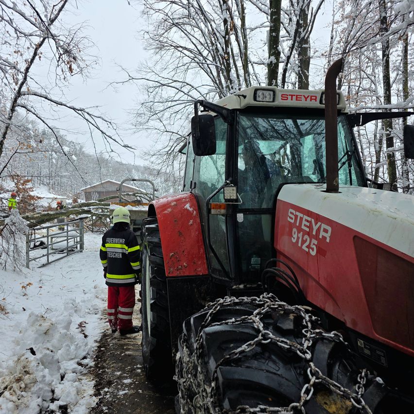 Ein Traktor mit Ketten an den Reifen, geparkt im Schnee. Ein Feuerwehrmann in voller Ausrüstung steht daneben.