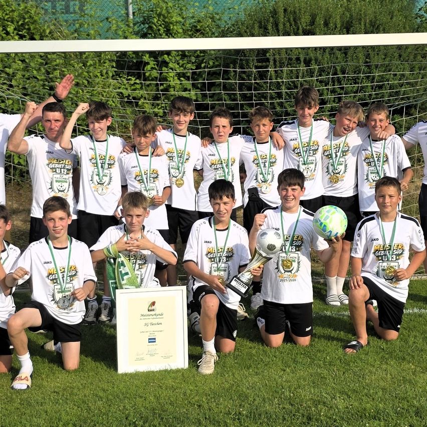 Eine Fußballmannschaft junger Jungen posiert mit ihren Trophäen und Medaillen vor einem Fußballtor.