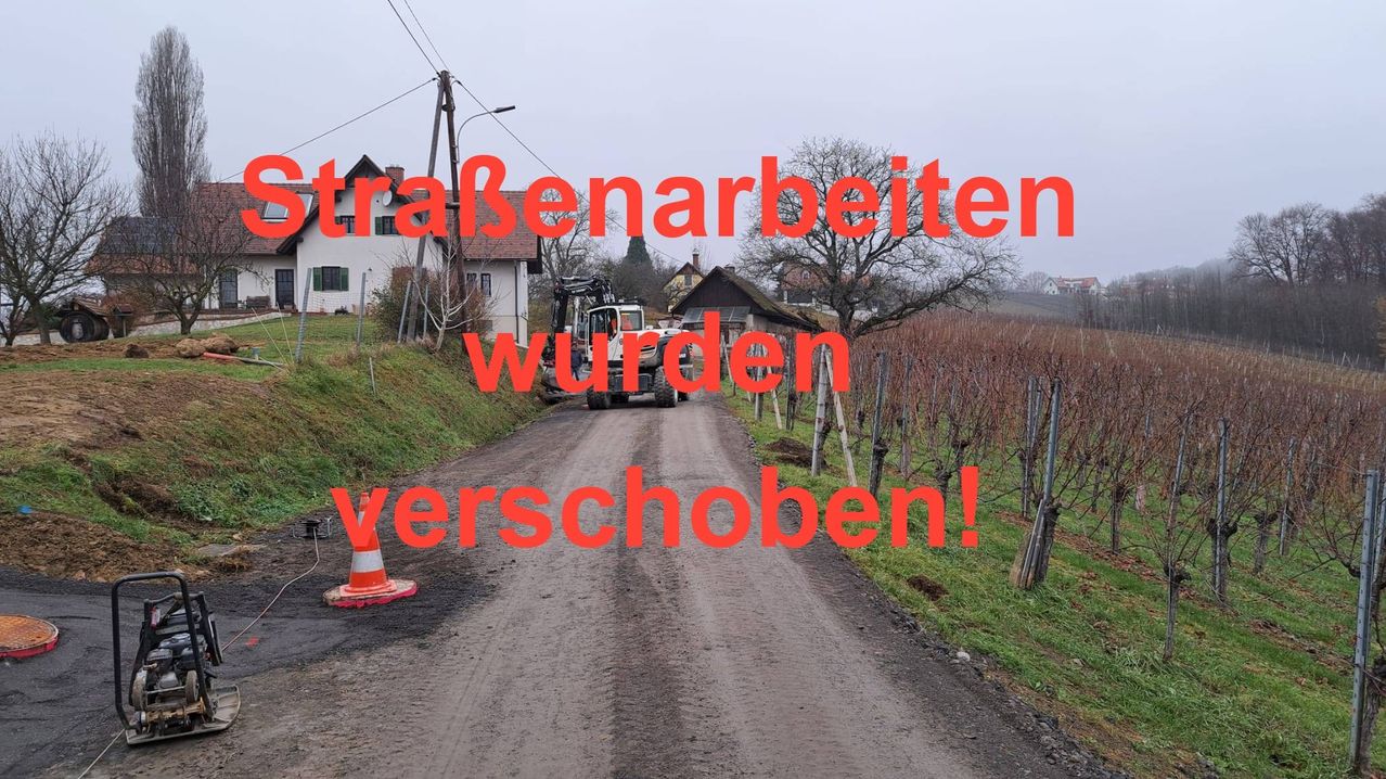A dirt road with a construction vehicle parked on it, surrounded by houses and trees. The text overlay reads 'Roadworks have been postponed!' in red.