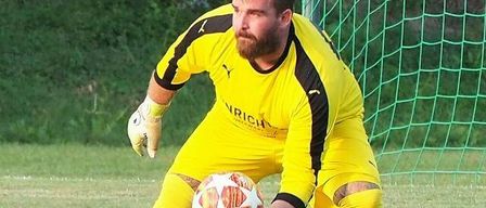 A soccer goalkeeper in a yellow jersey holds a soccer ball, poised to defend the goal, with a blurred background.