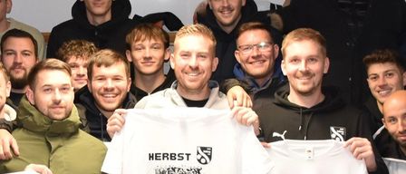 Eine Gruppe von Menschen, die weiße T-Shirts mit den Texten 'HERBST' und 'MEISTER' tragen, feiert freudig, wahrscheinlich für einen Meisterschaftssieg. Das Bild hat einen roten Rand mit dem Text 'Herbstmeister Asko Jabing'.