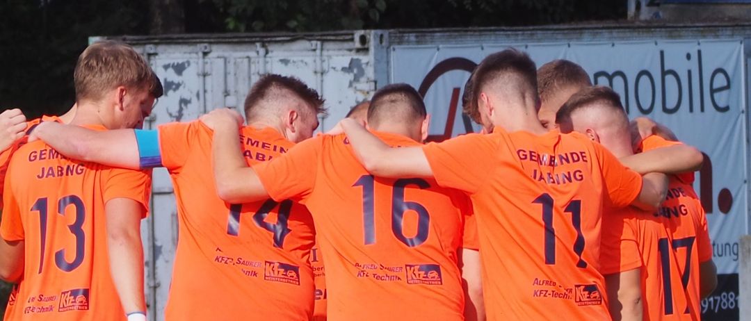 Eine Gruppe von Fußballspielern in orangefarbenen Trikots steht auf einem Feld. Die Nummern auf ihren Trikots reichen von 11 bis 17.