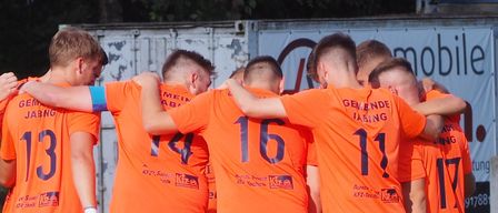 A group of soccer players wearing orange uniforms are huddled together on a field. The numbers on their jerseys range from 11 to 17.