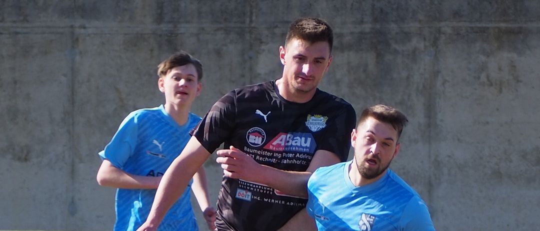 Three soccer players are on a field. Two are in blue shirts, one in black. They are playing soccer.