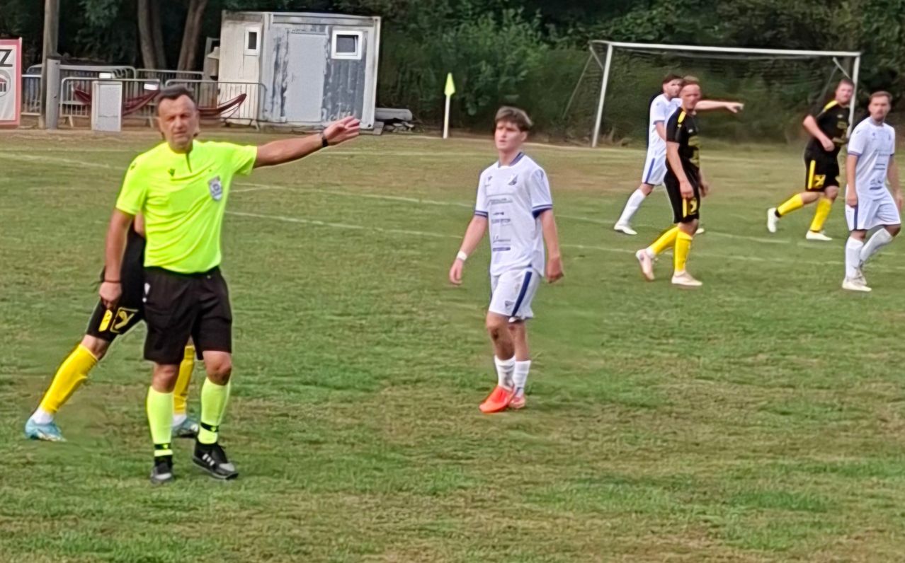 Ein Fußballschiedsrichter signalisiert einen Foul, während Spieler zweier Teams auf einem Rasenfeld spielen.