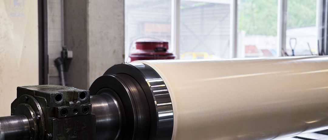 Eine große Rolle Material wird in einer Fabrik bearbeitet, mit Fenstern, die Bäume draußen zeigen.