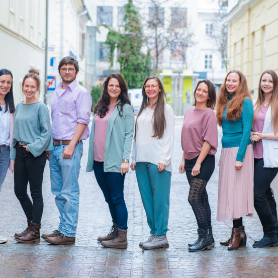 Eine Gruppe von acht Personen, darunter Männer und Frauen, steht in einer Reihe auf einer Kopfsteinpflasterstraße. Sie alle lächeln und posieren für ein Foto.