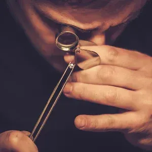 Eine Person benutzt eine Lupe, um ein kleines Objekt, möglicherweise ein Edelstein, in ihrer Hand genau zu untersuchen.