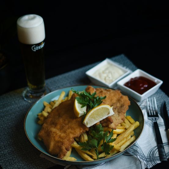 Ein Teller mit gebratenem Fisch und Pommes Frites mit einem Glas Bier und Beilagen.