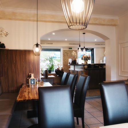 Ein Restaurantinnenraum mit Holzstühlen und -tischen, einer Holzbank und einer Bartheke mit Pflanze und hängenden Lampen.