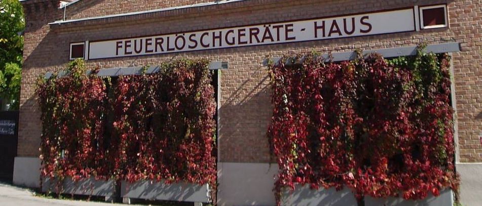 Ein Ziegelgebäude mit einem Turm obenauf und einem Schild mit der Aufschrift Feuerloschgerate Haus, das mit roten Reben an der Vorderseite bedeckt ist.