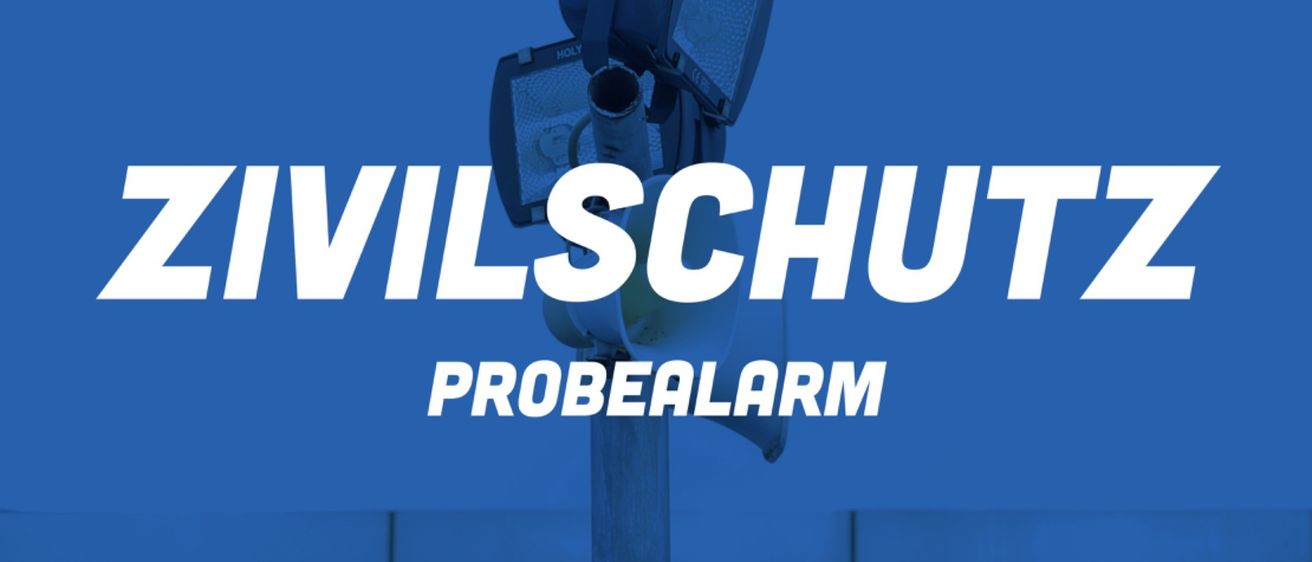 Ein Plakat mit einer Überwachungskamera und Scheinwerfern auf einem Pfosten, mit dem Text 'Civilschutz Probealarm' auf einem blauen Hintergrund.