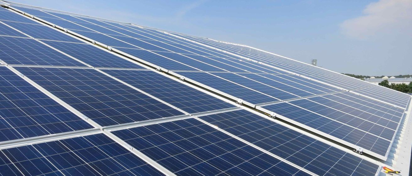 Eine Nahaufnahme einer großen Anordnung von Solarmodulen auf einem Gebäudedach unter einem klaren blauen Himmel.