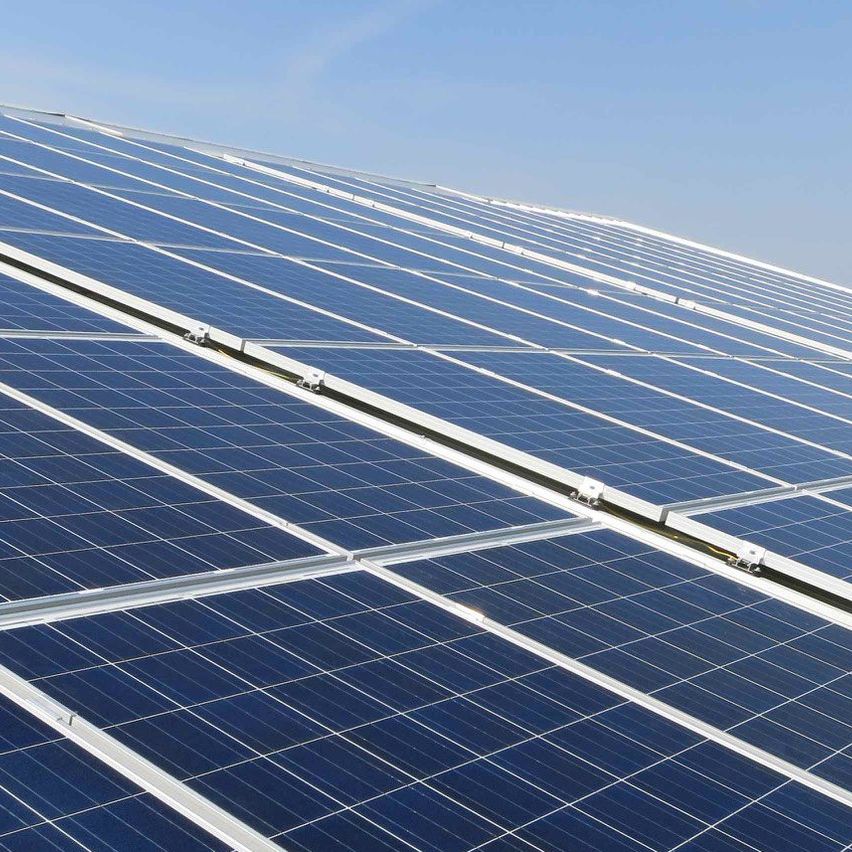 Eine Nahaufnahme einer großen Anordnung von Solarmodulen auf einem Gebäudedach unter einem klaren blauen Himmel.