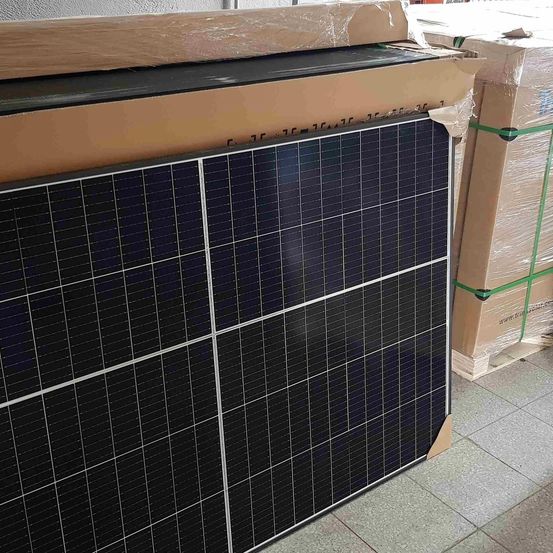 Ein Solarpanel mit mehreren Abschnitten ist auf einem Paletten gestapelt. Es ist in Plastik und braune Pappe eingewickelt. Dahinter befinden sich weitere verpackte Kisten.