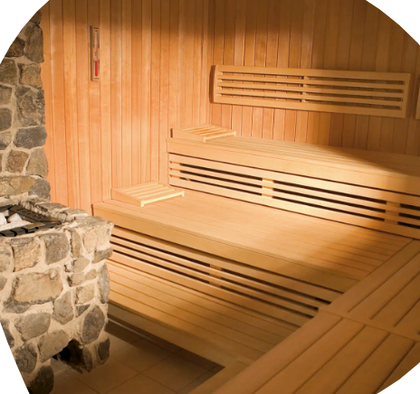 Ein Saunaraum mit Holzwänden und Bänken, ausgestattet mit einem Steinkamin und einer Temperaturanzeige an der Wand.