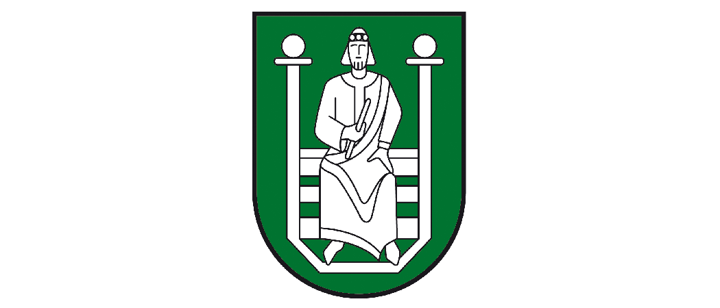 Ein grüner Schild mit einer sitzenden Figur in der Mitte, die eine Krone trägt und ein Buch hält. Die Figur sitzt auf einer Bank, die von zwei Säulen gestützt wird.