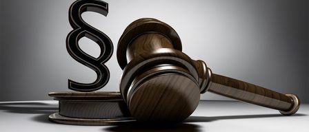 Ein hölzerner Hammer mit dem Buchstaben S auf einem hölzernen Block vor grauem Hintergrund.