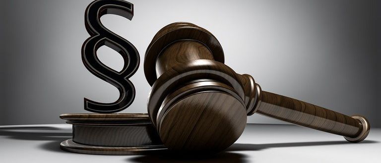 A wooden gavel with the letter S on top of a wooden block against a gray background.