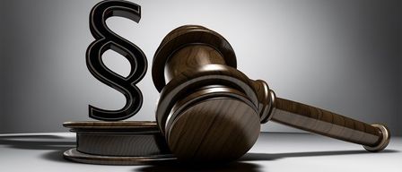 Ein hölzerner Richterhammer mit dem Buchstaben S darauf steht auf einem hölzernen Block auf einer weißen Oberfläche.