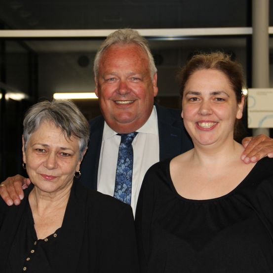 Drei Menschen, ein Mann und zwei Frauen, lächeln und posieren für ein Foto.